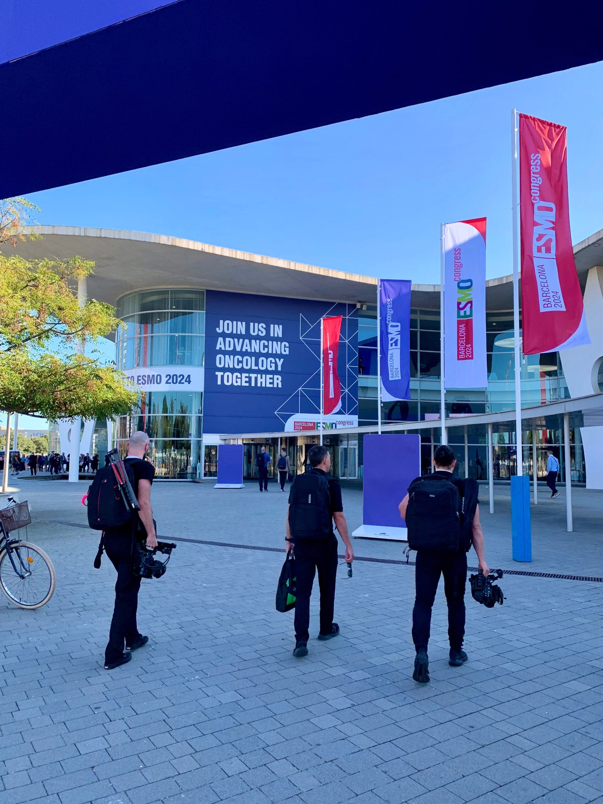 Crew approaching entrance of ESMO 2024 conference, with signage reading ‘Join us in advancing oncology together.