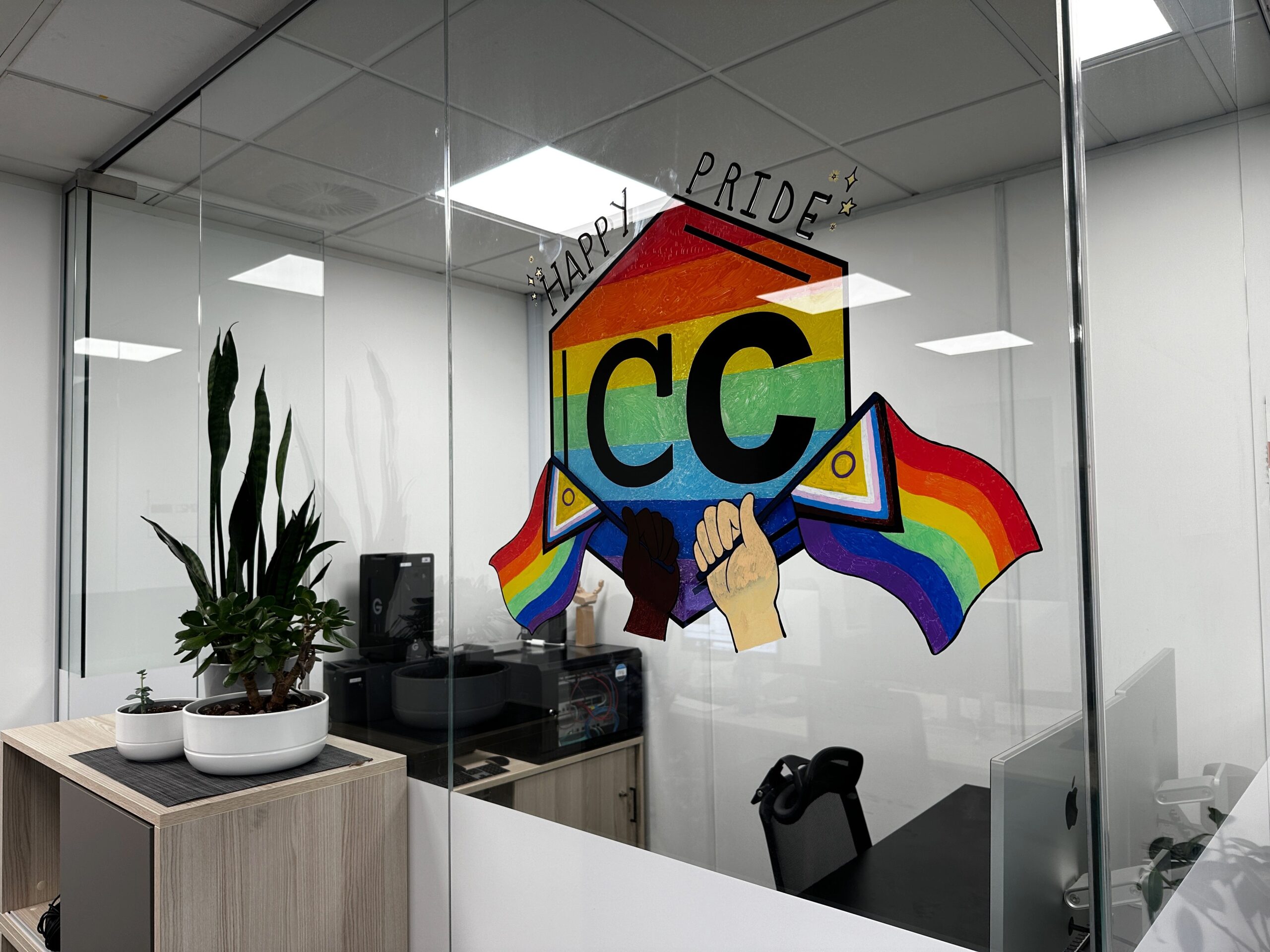 Woman drawing a rainbow-coloured ICC logo on a glass office wall.